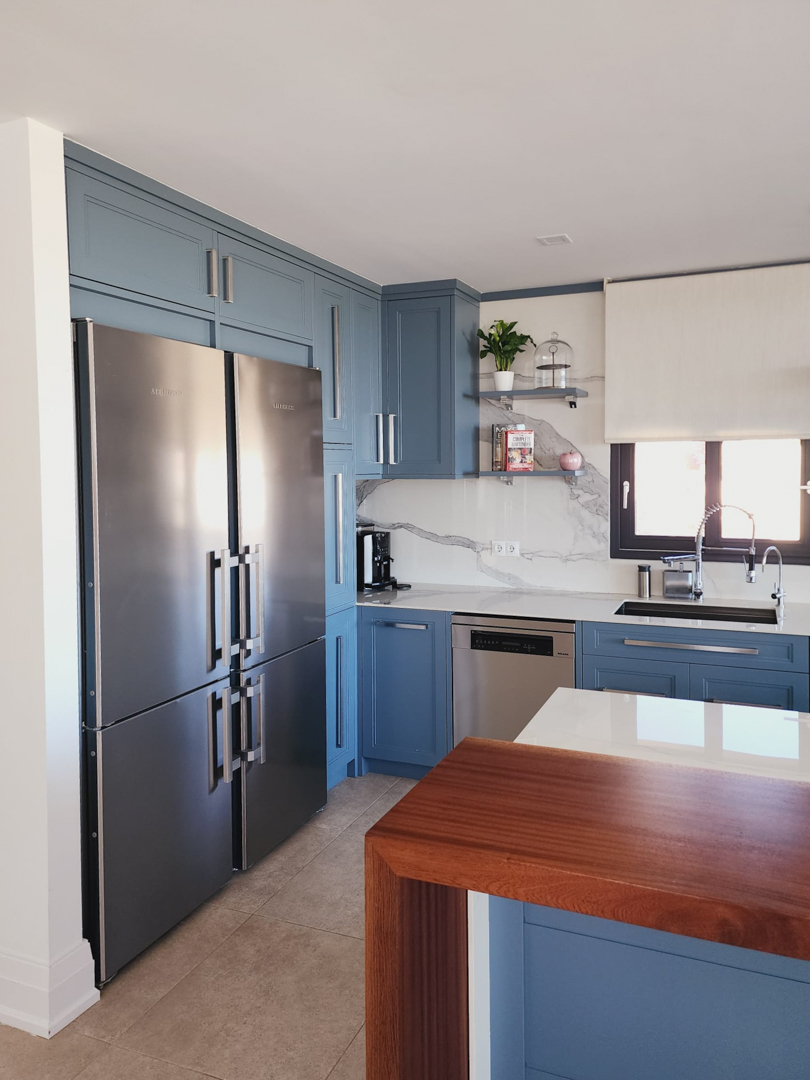 Cuisine moderne aux meubles bleu pastel, crédence effet marbre et électroménager en inox. Un plan de travail en bois massif apporte une touche chaleureuse.