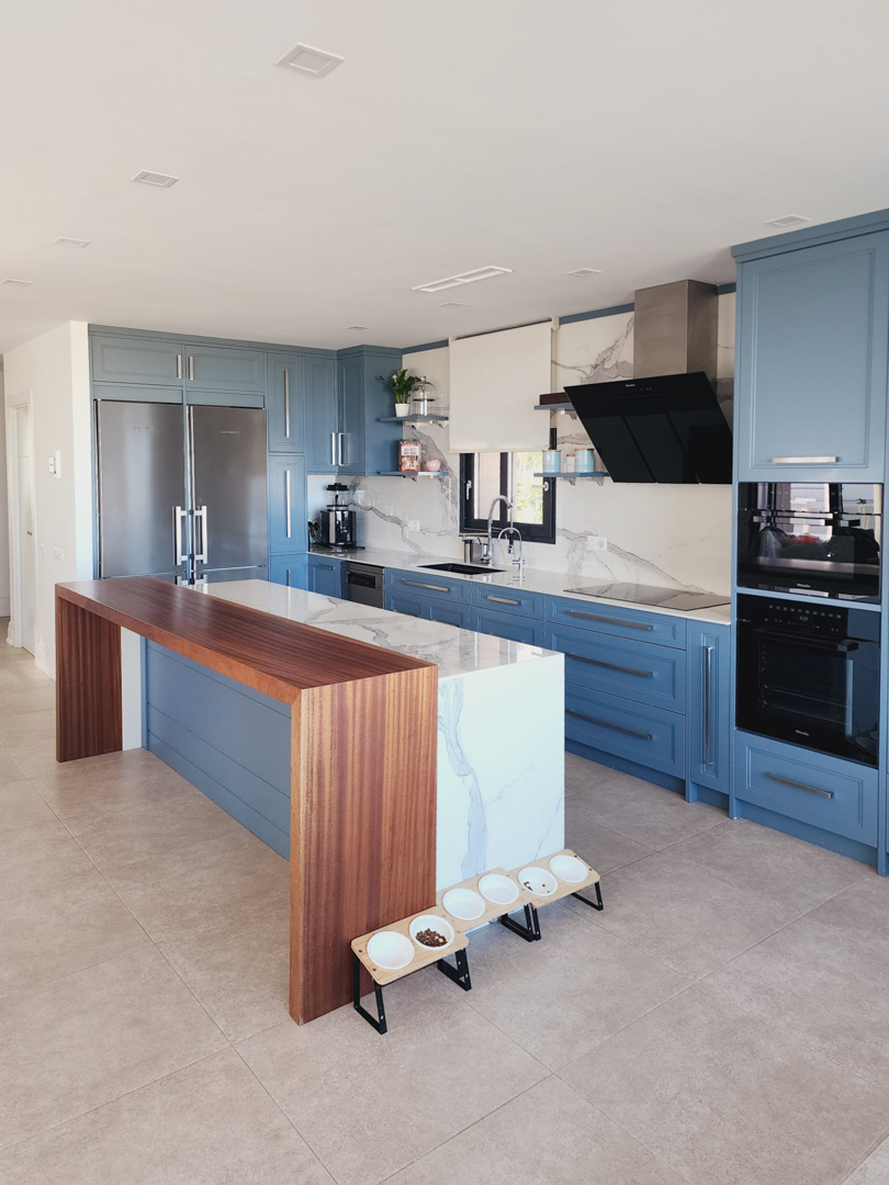 Cuisine moderne aux meubles bleus, dotée d'un îlot en marbre avec bar en bois intégré. Équipée d'appareils Miele et d'une crédence en pierre naturelle assortie.