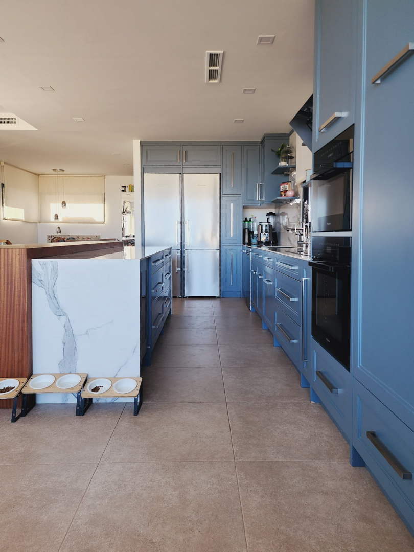 Cuisine moderne avec des meubles bleu pastel, un îlot central en marbre veiné et des appareils Miele intégrés. Sol en grès cérame et climatisation par conduits.
