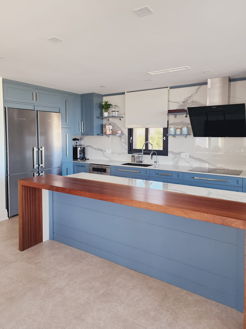 Cuisine moderne avec meubles bleus, plans de travail effet marbre et bar en bois massif. Elle dispose d'appareils intégrés et d'un espace de travail spacieux et lumineux.
