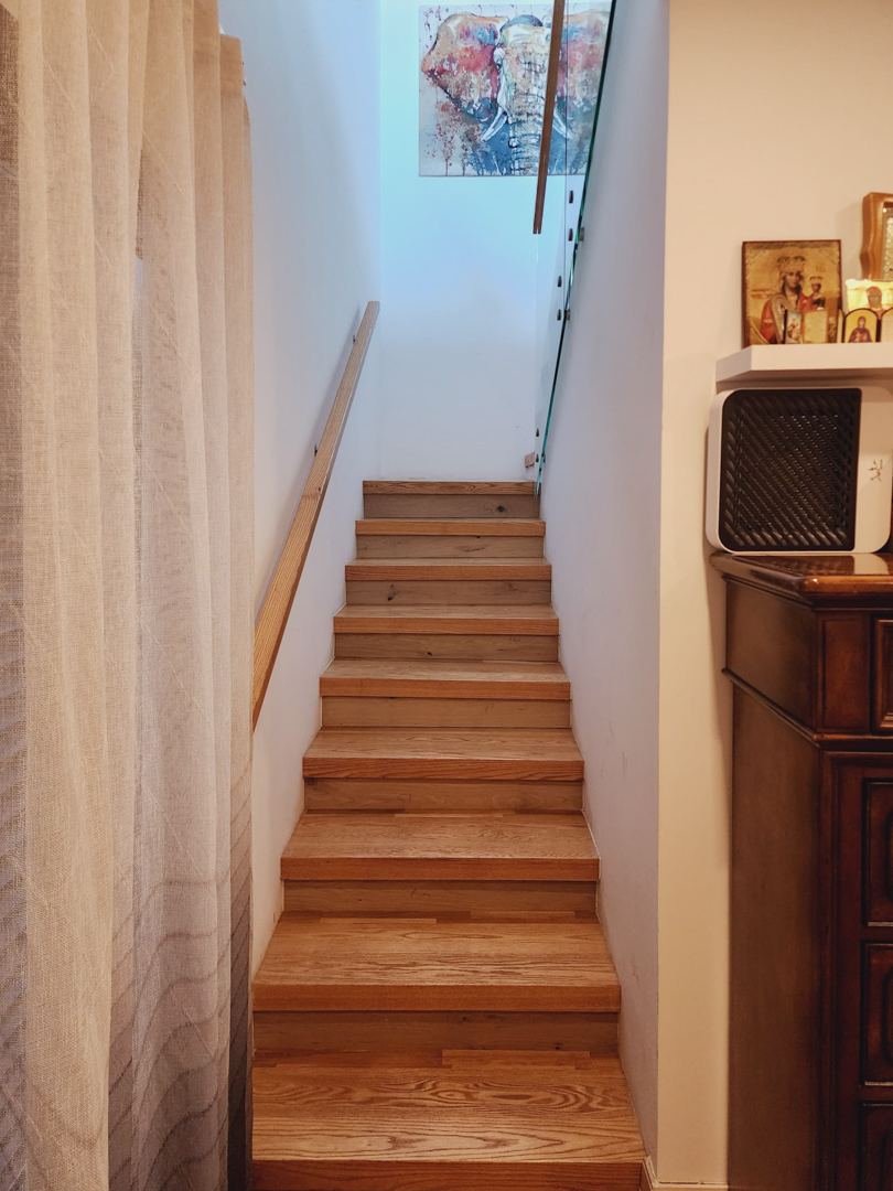 Escalier intérieur en bois avec main courante assortie et garde-corps en verre, éclairé par une lumière naturelle zénithale et décoré d'art mural.