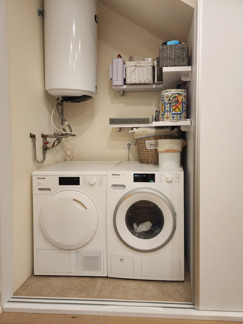 Espace buanderie équipé d'un lave-linge et d'un sèche-linge Miele, d'un chauffe-eau solaire et d'étagères de rangement optimisées.