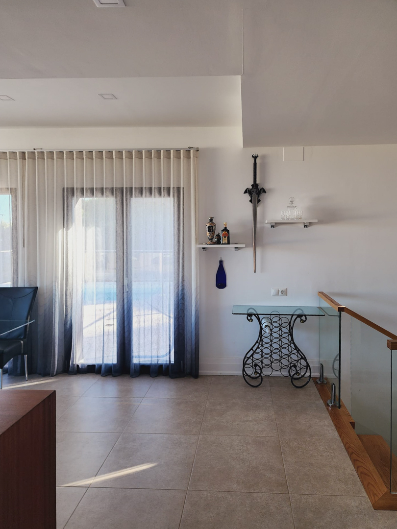 Espace de vie lumineux avec sol en grès cérame, console décorative en fer forgé et verre, et escalier moderne avec garde-corps vitré et finitions bois.