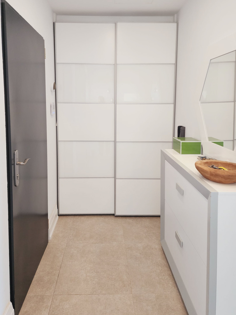 Hall d'entrée avec placard intégré à portes coulissantes blanches, commode design et carrelage au sol aux tons naturels.