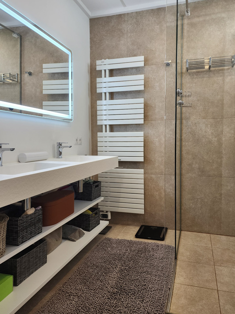 Salle de bain moderne avec double vasque intégrée, étagères ouvertes et miroir rétroéclairé par LED. Comprend un radiateur sèche-serviettes blanc et une douche à l'italienne.
