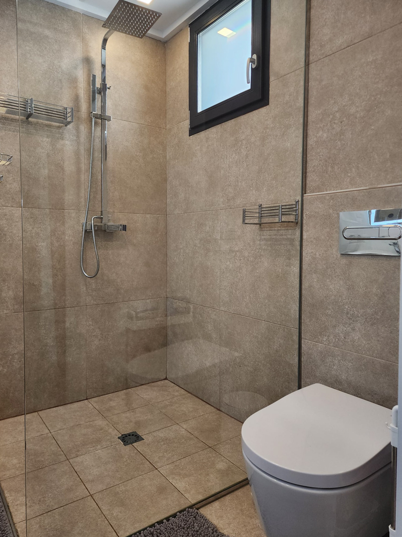 Salle de bain moderne avec douche à l'italienne, paroi en verre, robinetterie chromée à effet de pluie et carrelage céramique aux tons sable naturels.