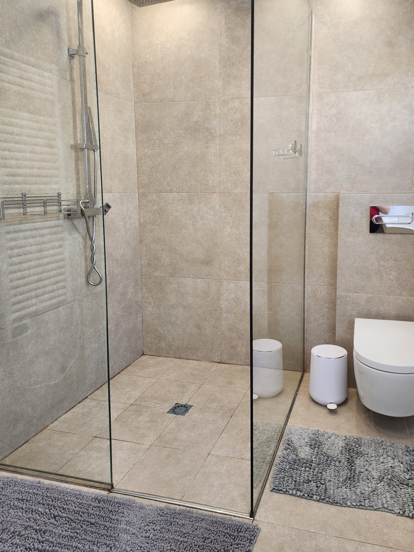 Salle de bains moderne avec douche à l'italienne, paroi en verre et carrelage en grès cérame beige. Équipée d'un WC suspendu et d'une robinetterie chromée.