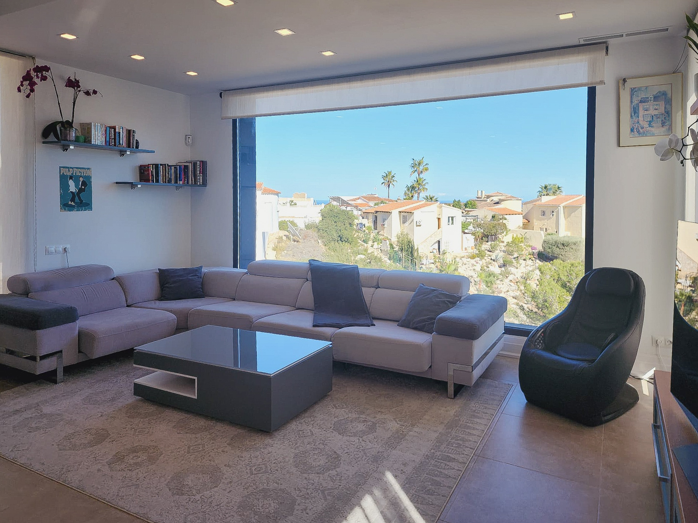 Salon moderne avec canapé en L, table basse minimaliste et grande baie vitrée. Comprend un éclairage de plafond encastré et une vue dégagée sur le paysage environnant.
