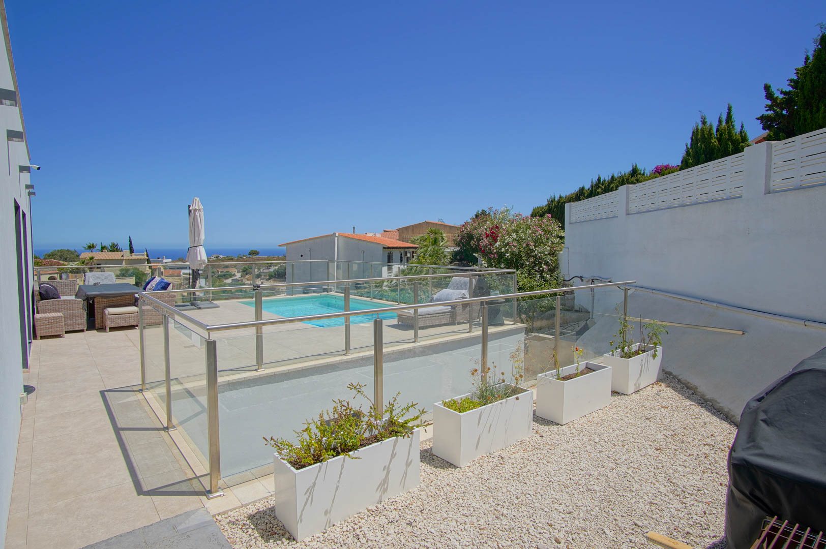 Terrasse extérieure avec garde-corps en verre et acier, piscine avec solarium et espace en gravier agrémenté de jardinières blanches modernes.