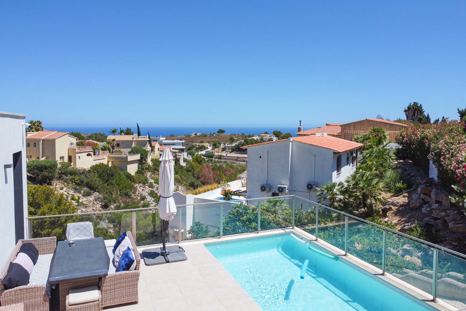 Terrasse extérieure avec piscine, garde-corps en verre et coin repas en rotin, offrant une vue panoramique sur la mer Méditerranée à Cumbre del Sol.