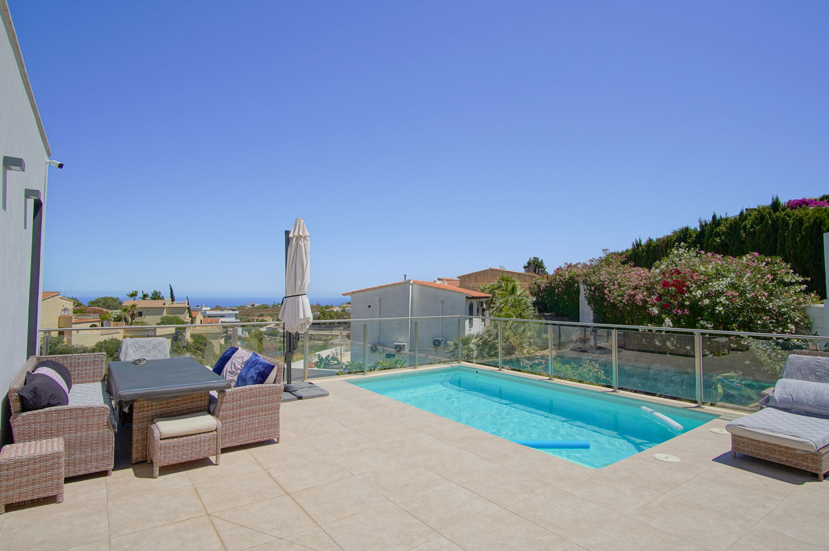 Terrasse extérieure avec piscine rectangulaire, garde-corps en verre et mobilier en rotin. L'espace orienté plein sud offre une vue dégagée sur la mer Méditerranée.