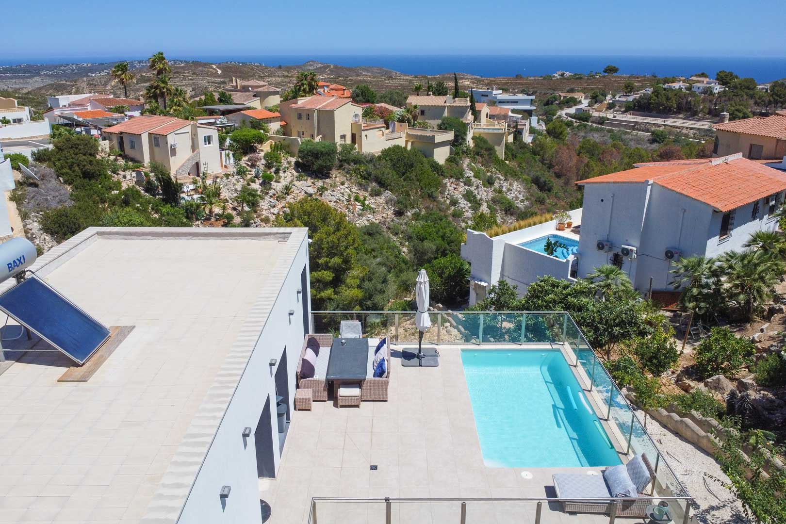 Vue aérienne de la terrasse avec piscine, garde-corps en verre et mobilier d'extérieur. Le toit plat dispose d'un panneau solaire avec vue dégagée sur la mer.