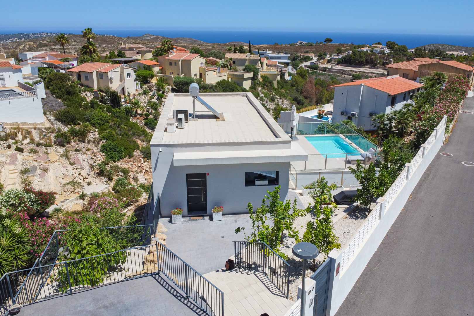 Vue aérienne de la villa moderne montrant le toit plat avec panneau solaire, la piscine privée sécurisée par du verre et le panorama sur la mer Méditerranée.