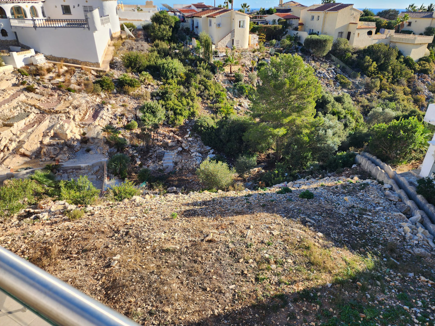 Vue depuis le balcon sur le terrain en pente de la parcelle, composé de gravier, de roches naturelles et de végétation méditerranéenne.