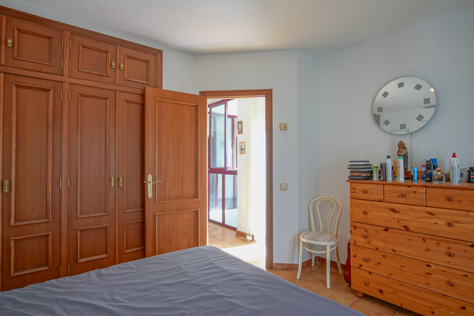 Chambre avec de grands placards encastrés en bois, une commode assortie et un sol en grès. La pièce s'ouvre sur un dégagement lumineux soulignant la menuiserie traditionnelle.