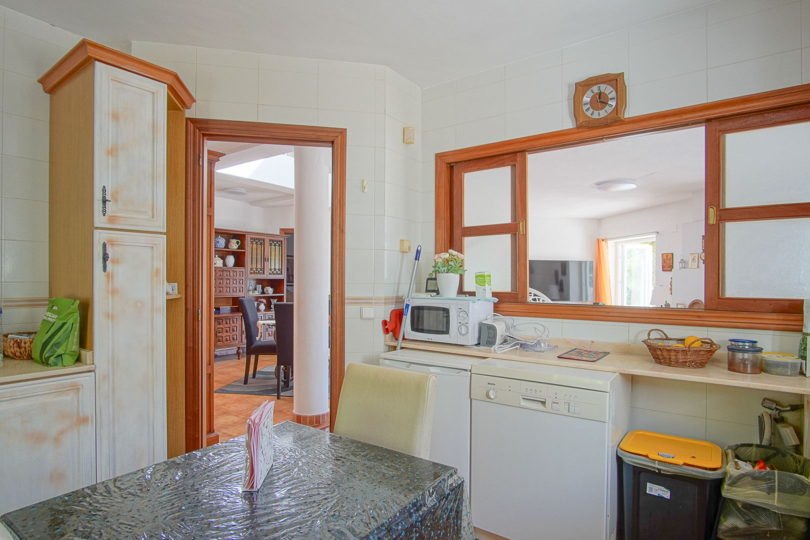 Cuisine indépendante avec mobilier rustique, coin petit-déjeuner et passe-plat vers la salle à manger. Équipée d'un lave-vaisselle et d'un plan de travail clair.