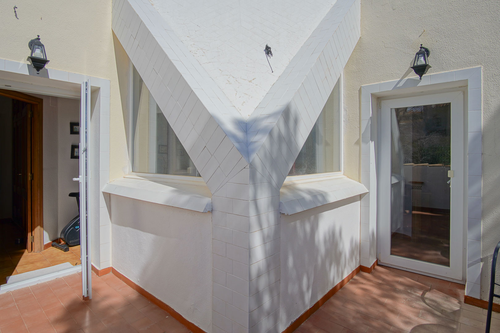 Détail architectural de la terrasse supérieure avec piliers en carrelage blanc, sol en terre cuite et accès direct aux pièces intérieures lumineuses.