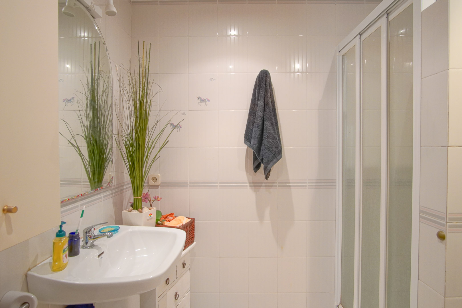 Salle de bain fonctionnelle avec murs carrelés blancs, lavabo en porcelaine, miroir cintré et douche équipée d'une porte coulissante.