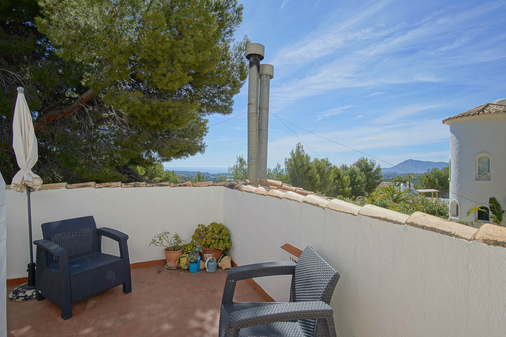 Terrasse à l'étage avec sol en terre cuite et fauteuils en résine, offrant une vue dégagée sur la mer Méditerranée et les montagnes environnantes.