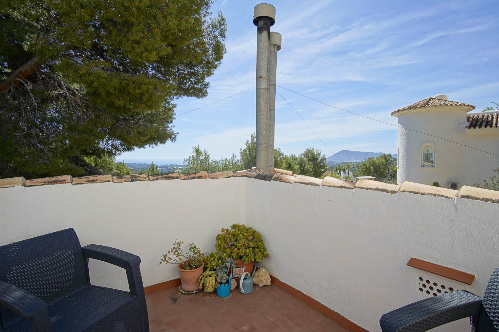 Terrasse à l'étage avec sol en terre cuite, offrant une vue dégagée sur la mer et les montagnes au milieu d'une pinède méditerranéenne.