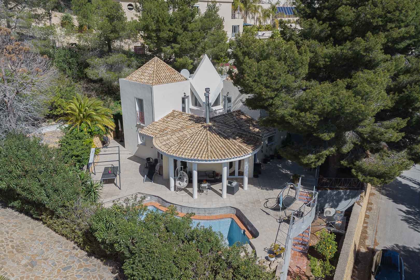 Vue aérienne de la villa avec son porche circulaire à colonnes blanches, sa piscine privée et ses terrasses en pierre entourées de pins et de jardins méditerranéens.