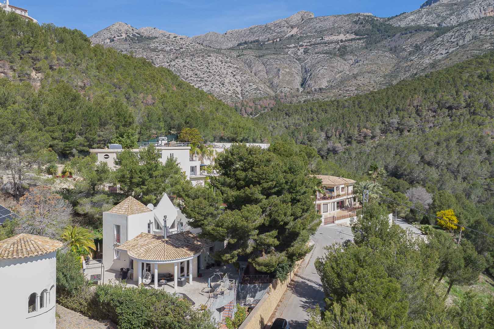 Vue aérienne de la villa révélant son architecture méditerranéenne et ses toits en tuiles, entourée d'une pinède dense avec les montagnes en arrière-plan.