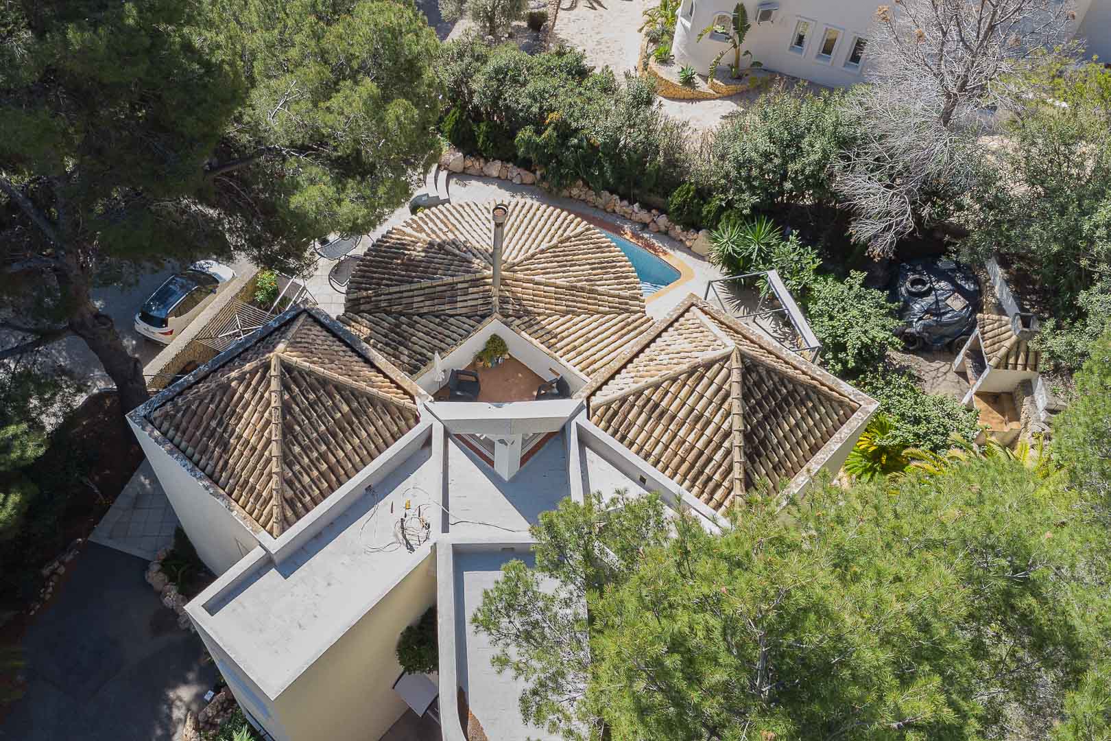 Vue aérienne révélant l'architecture originale de la villa avec ses toits en tuiles, une cheminée centrale et une terrasse nichée entre les structures supérieures.