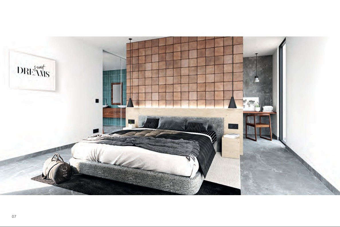 Chambre principale avec mur d'accent en carreaux de terre cuite, tête de lit en bois rétroéclairée et salle de bain attenante visible derrière une paroi vitrée.