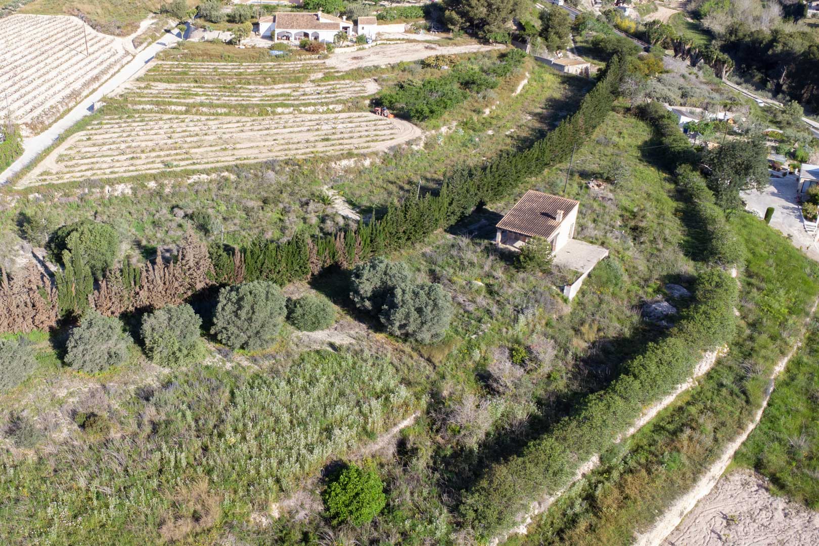 Vue aérienne de la parcelle de 10 920 m2 à Teulada, illustrant le terrain en terrasses avec sa végétation méditerranéenne et une petite construction rurale.