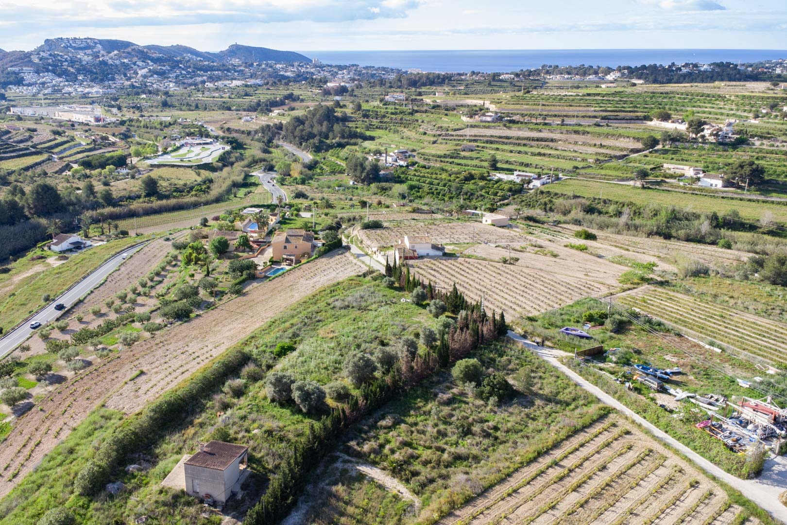 Vue aérienne de la vaste parcelle rustique de 10 920 m2 à Teulada-Moraira, avec ses terrasses agricoles et une vue dégagée sur la mer Méditerranée.