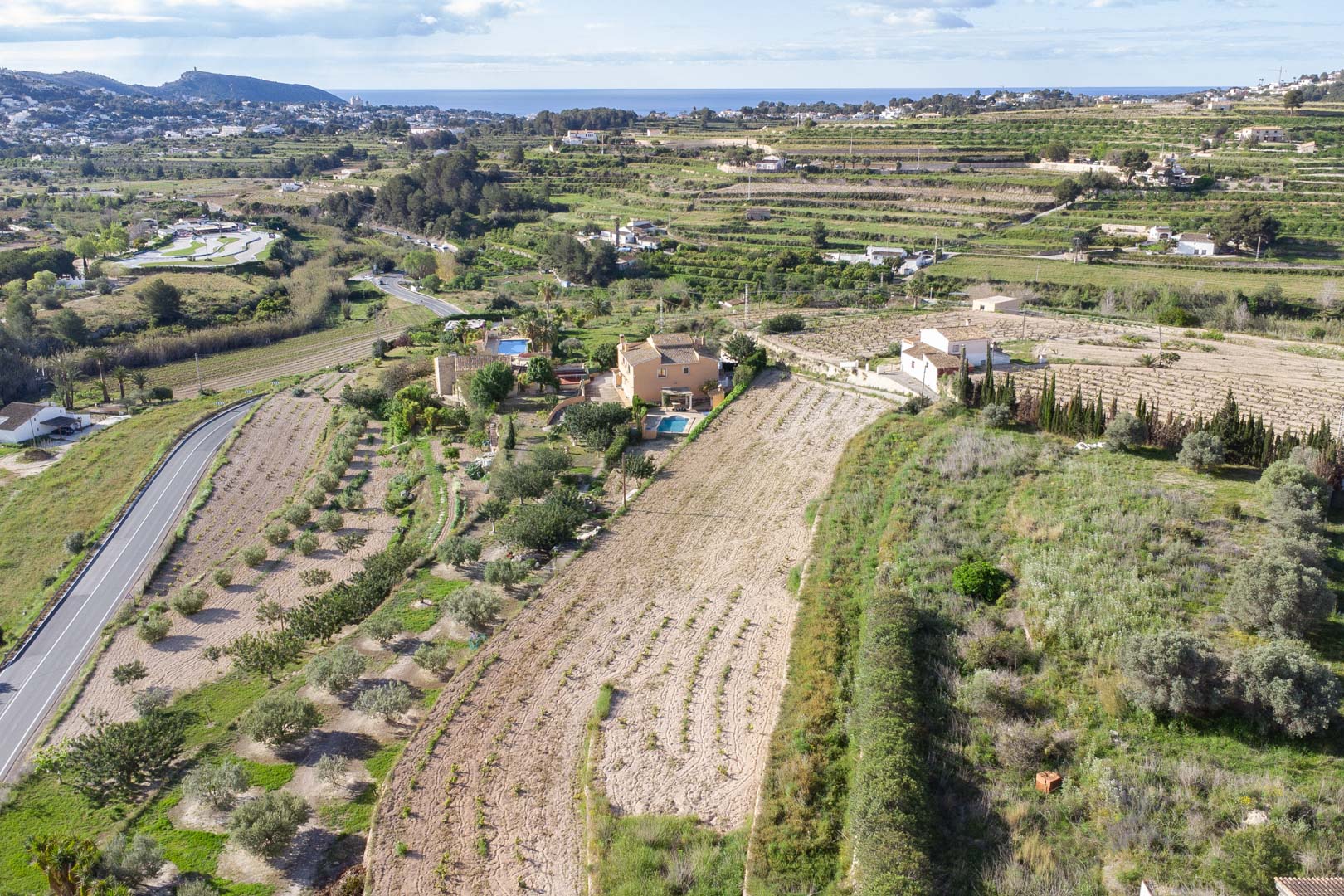 Vue aérienne du vaste terrain de 10 920 m2 à Teulada-Moraira, illustrant les terrasses agricoles et les vues panoramiques sur la côte méditerranéenne.
