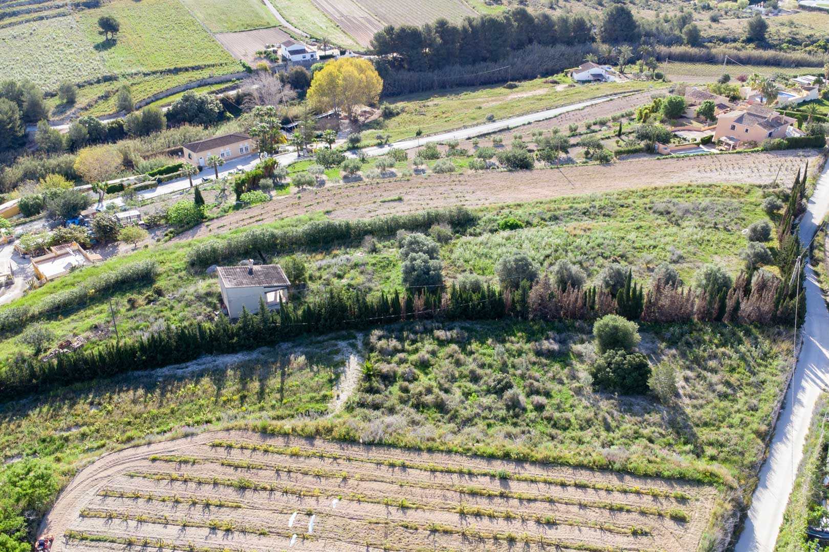 Vue aérienne du vaste terrain rustique à Teulada, présentant des terrasses avec une végétation méditerranéenne et une petite structure existante.