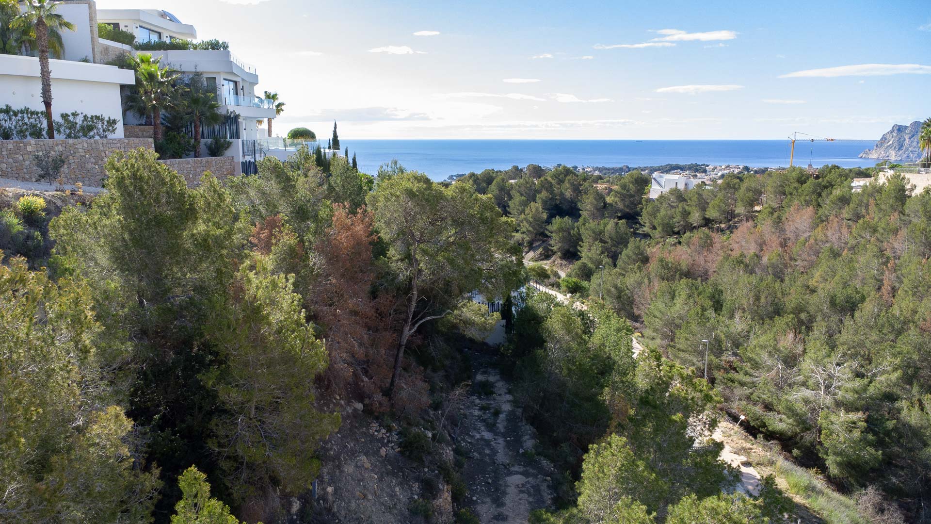 Vues panoramiques sur la mer Méditerranée et le Peñón de Ifach depuis le terrain surélevé, entouré de pinèdes et de villas contemporaines.