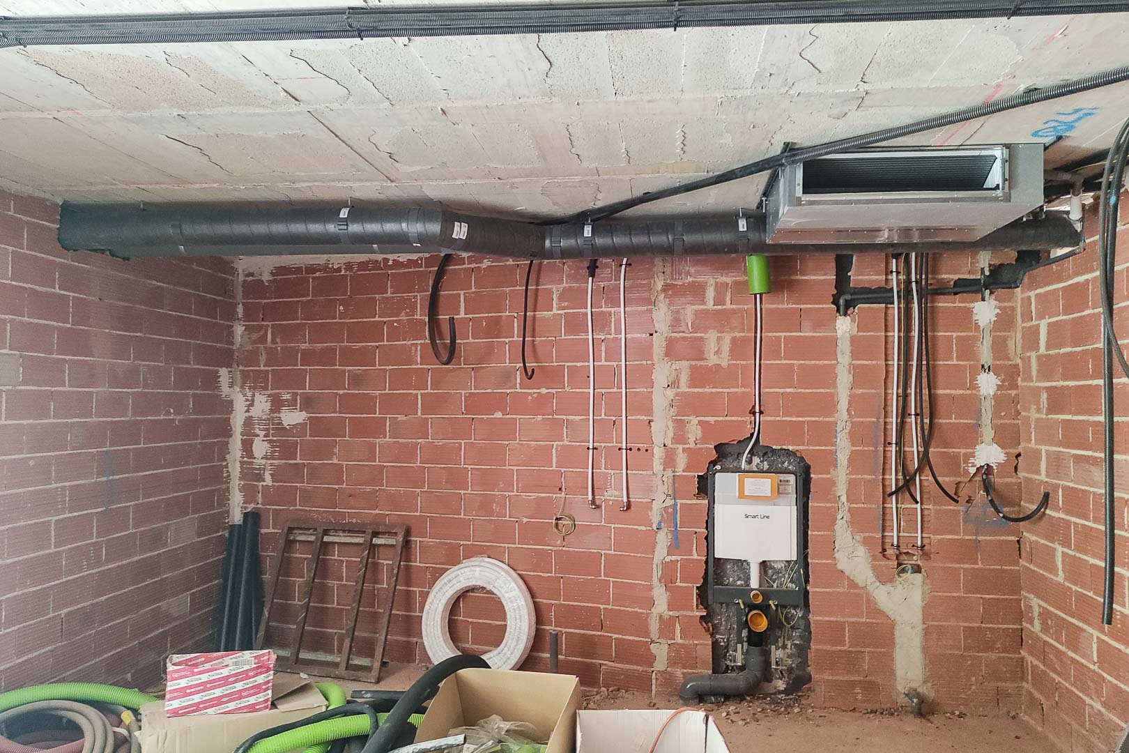 Détail de la phase de construction illustrant l'installation du système de climatisation par aérothermie et le bâti-support pour WC suspendu sur briques.