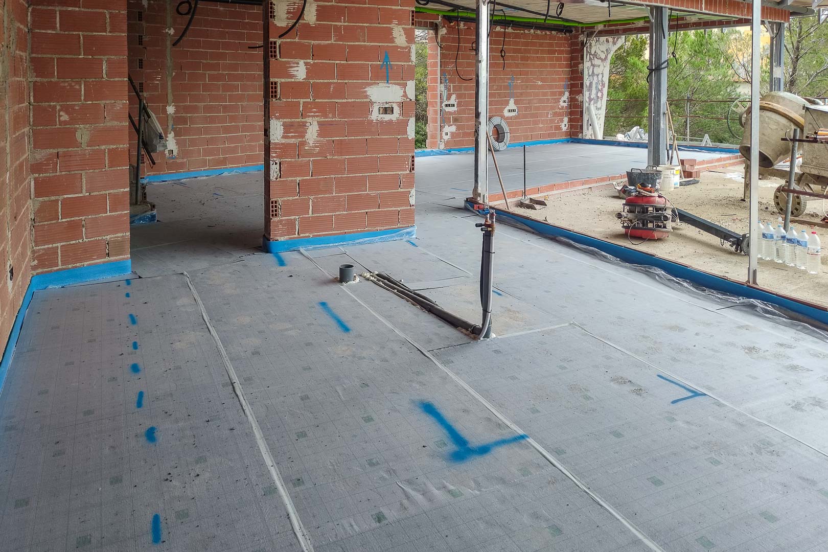 État d'avancement des travaux avec pose de la membrane isolante au sol et attentes de plomberie pour le futur chauffage radiant.