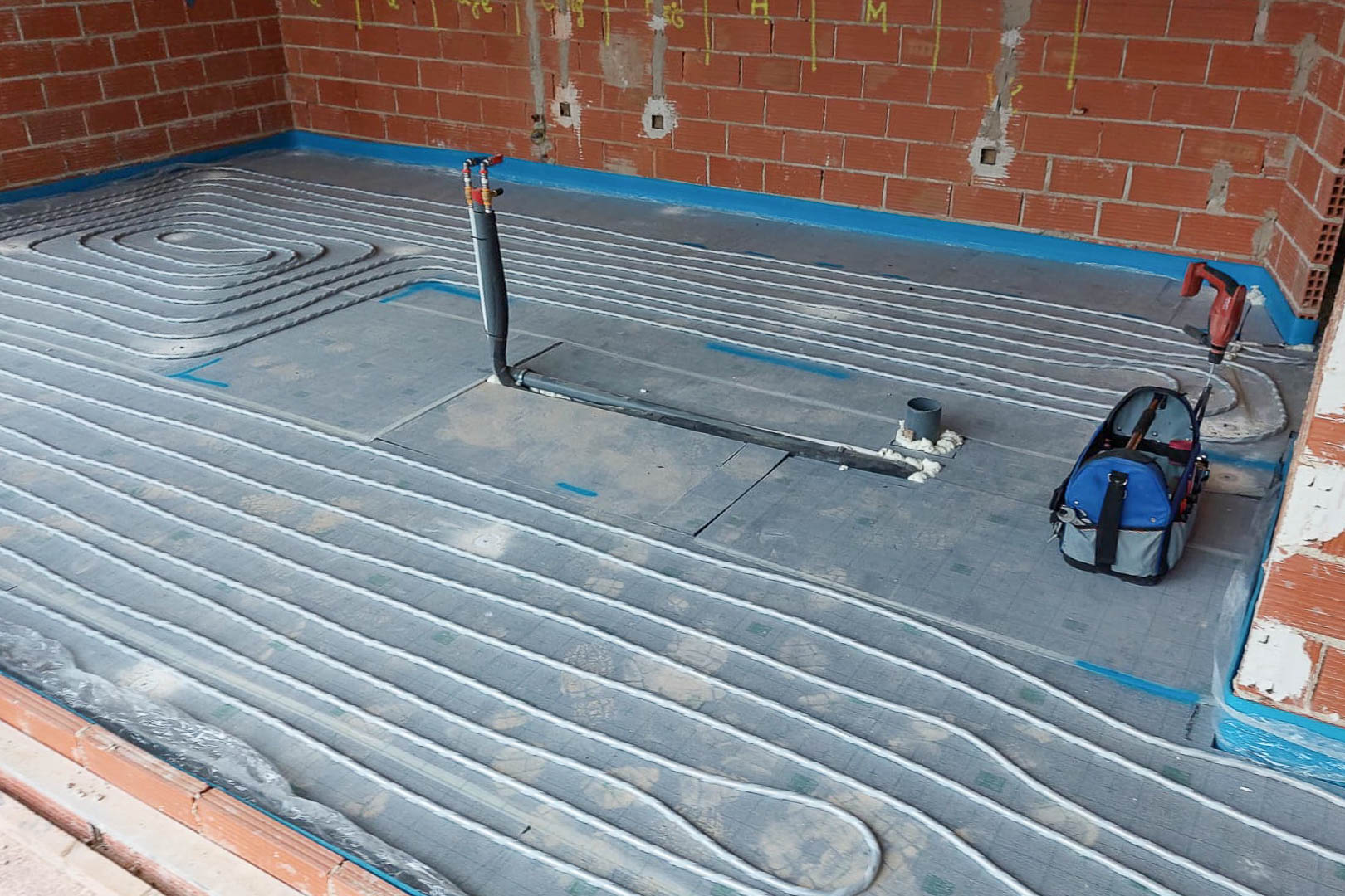 Installation technique du chauffage au sol, montrant la disposition des tuyaux radiants sur des panneaux isolants dans une pièce en phase de gros œuvre.