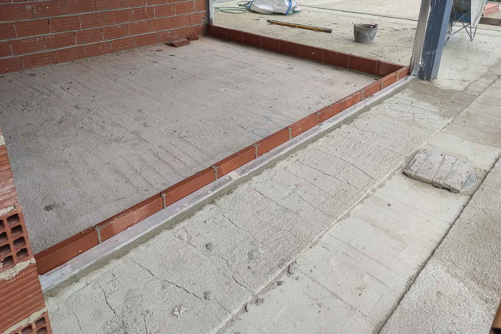 Phase de construction : détail du nivellement de la dalle et pré-installation des rails métalliques pour les grandes baies vitrées coulissantes.