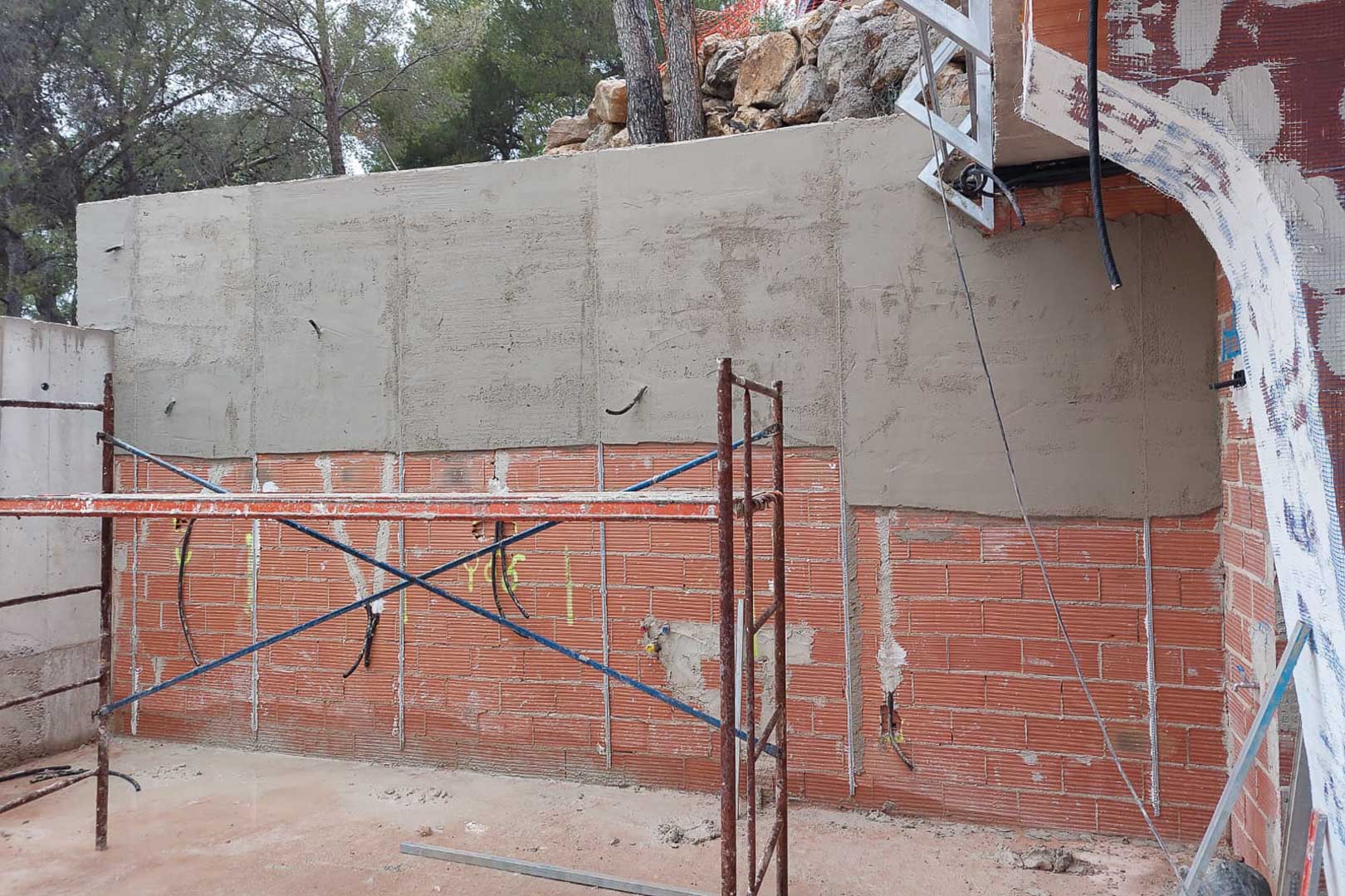 Phase de construction : enduit des murs en briques, pré-installations électriques et échafaudage technique sur la structure extérieure.