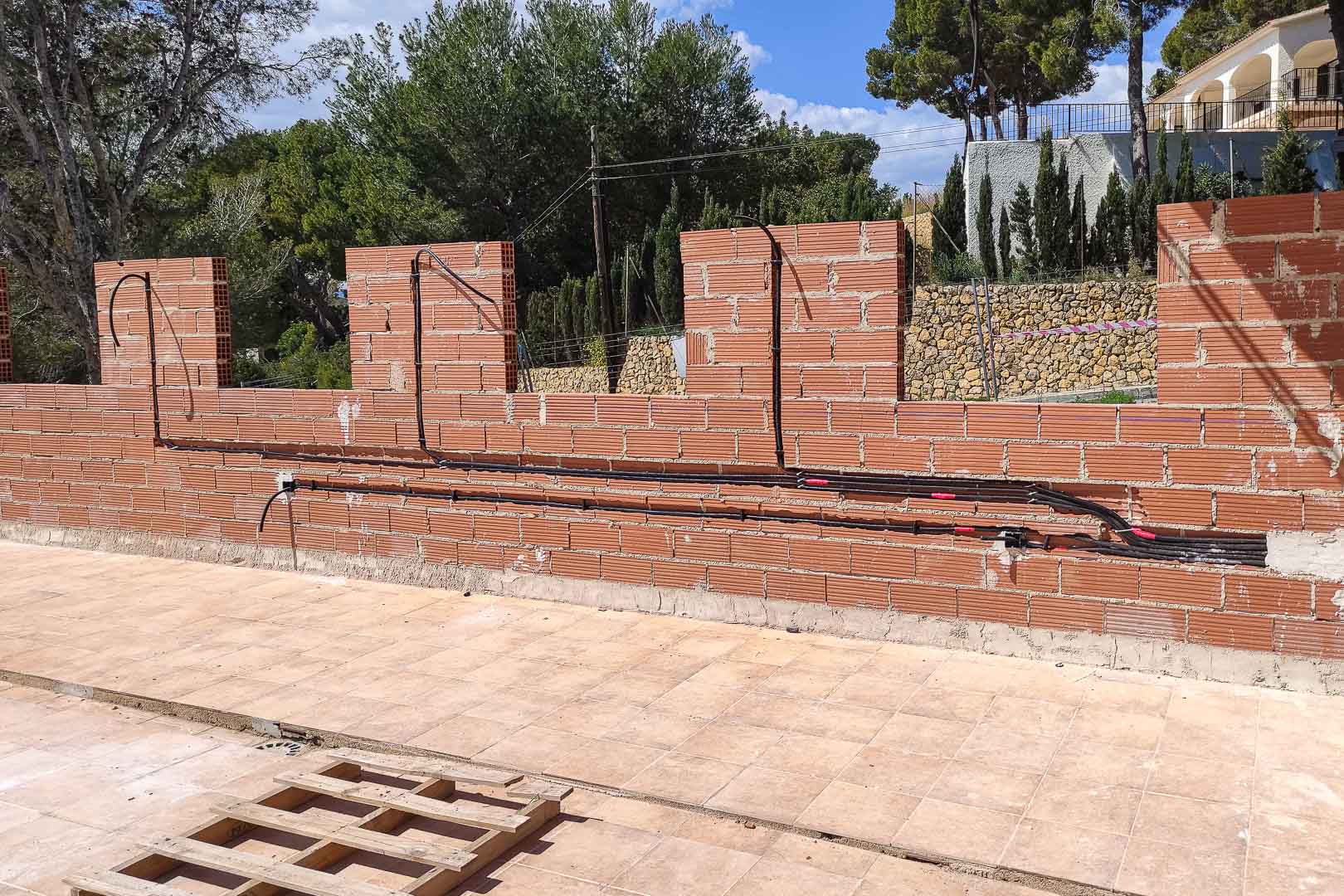 Phase de construction montrant l'installation de conduits électriques sur les murs en briques, préparant l'éclairage extérieur et la domotique.