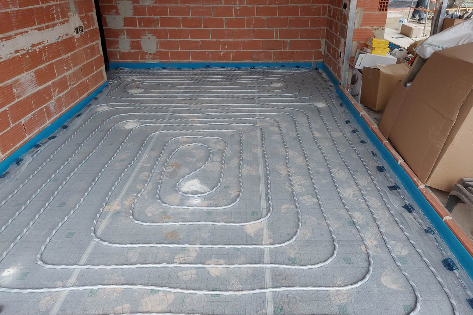 Phase d'installation du système de chauffage au sol avec tuyauterie en spirale sur panneaux isolants et bande périphérique.