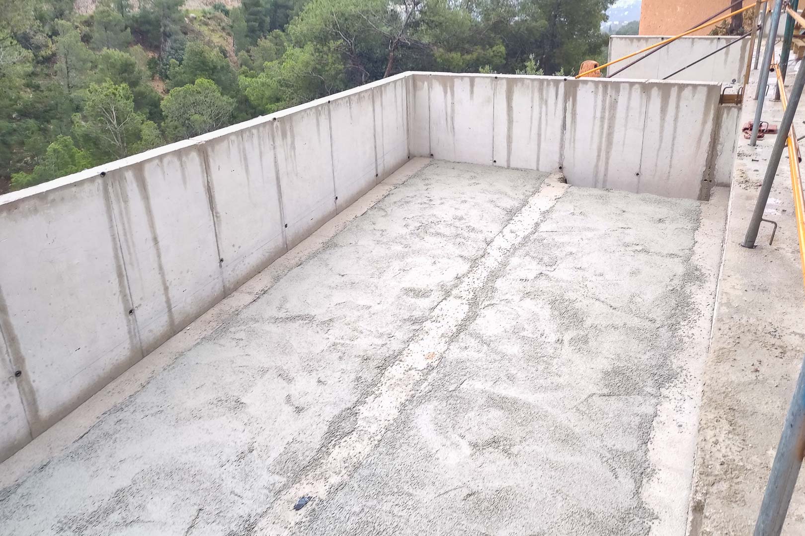 Structure en béton armé en cours de construction, présentant les murs périmétriques et la dalle d'une future terrasse avec vue sur la forêt de pins.