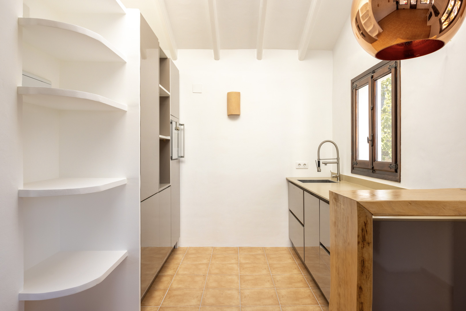 Cuisine lumineuse avec étagères intégrées blanches, armoires grises et plan de travail en bois. Sol en carreaux rustiques.