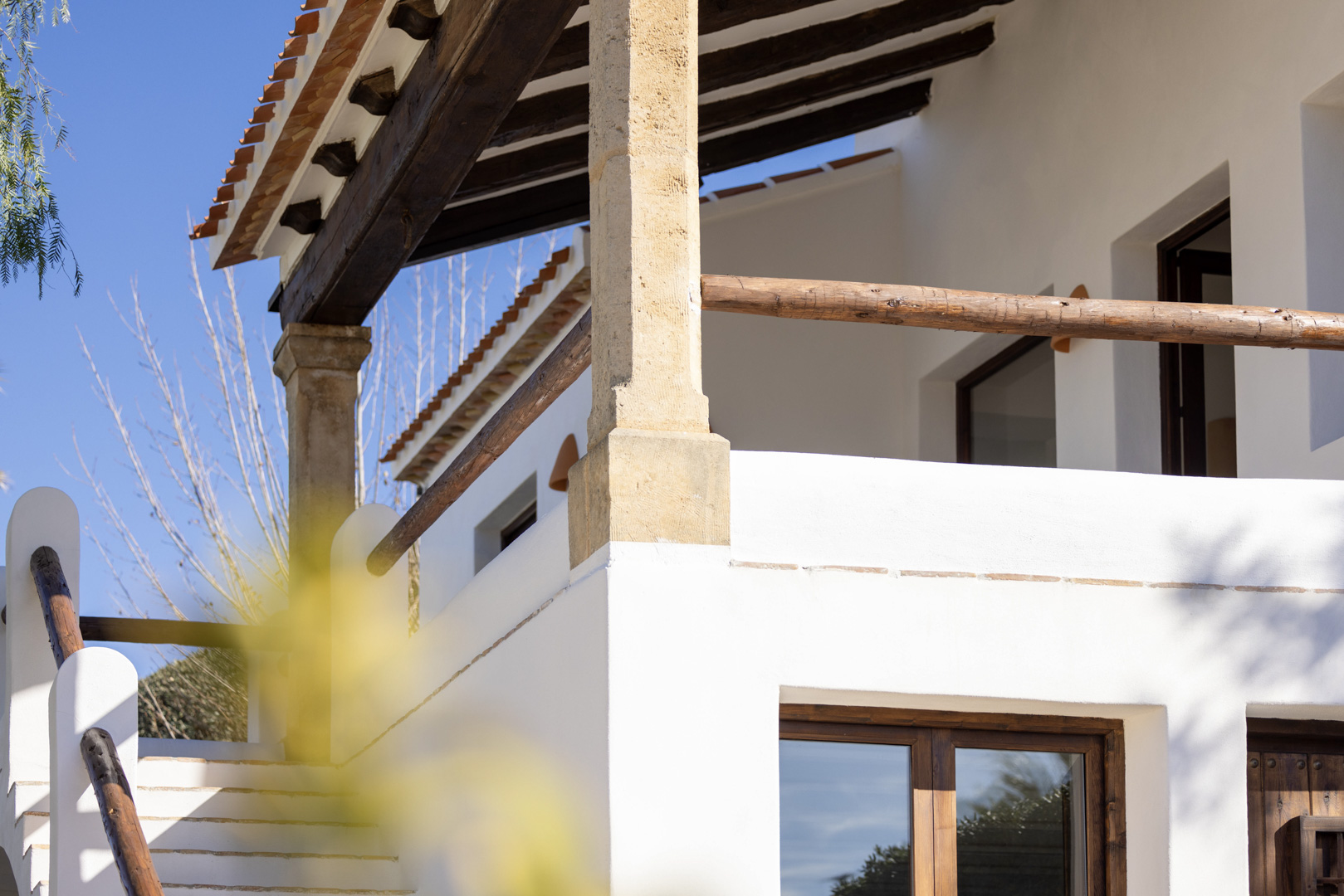 Détail architectural de la villa : porche avec poutres en bois et rambarde rustique, escalier extérieur en pierre blanche.