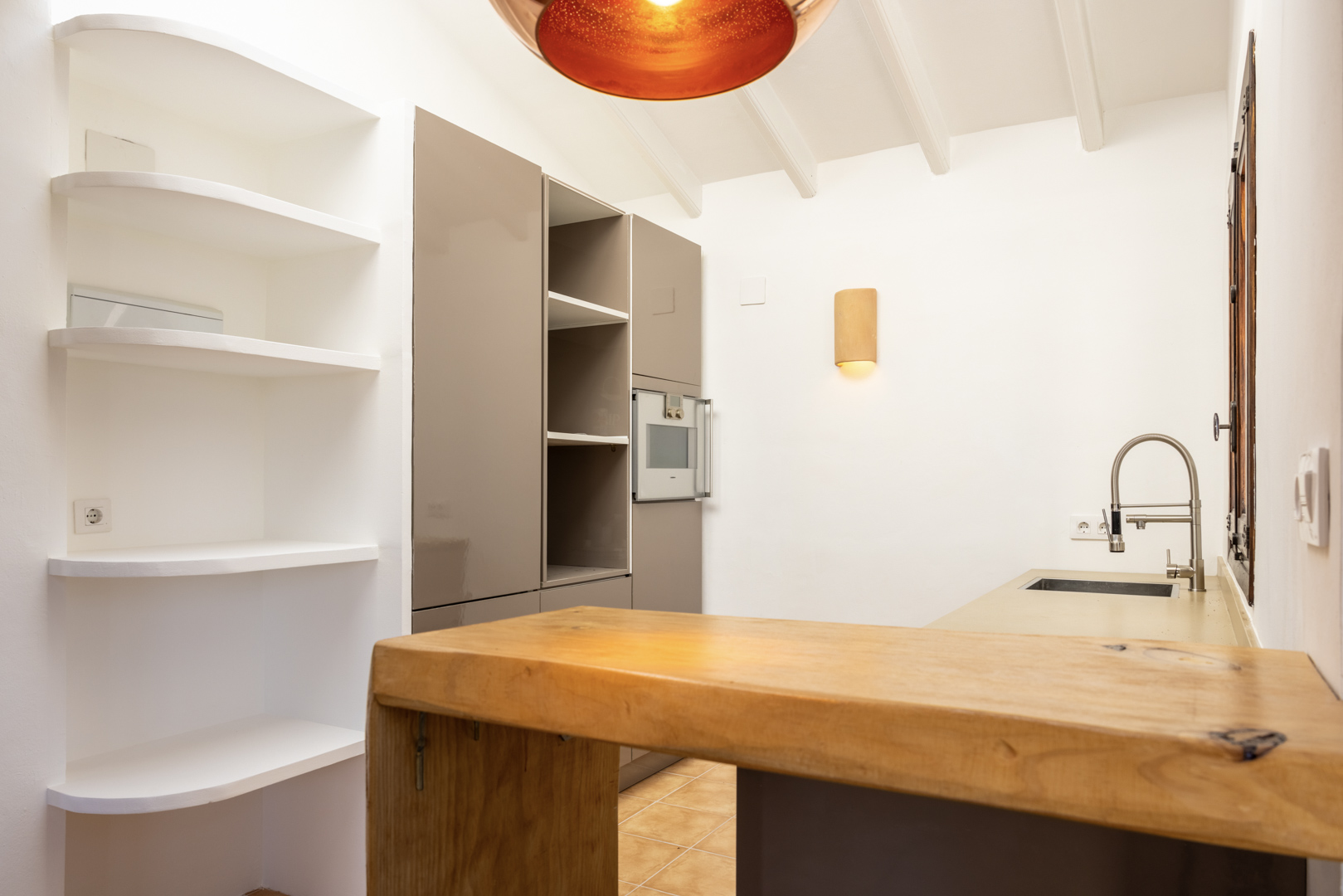 Détail de cuisine avec îlot en bois, étagères blanches et éclairage chaleureux.