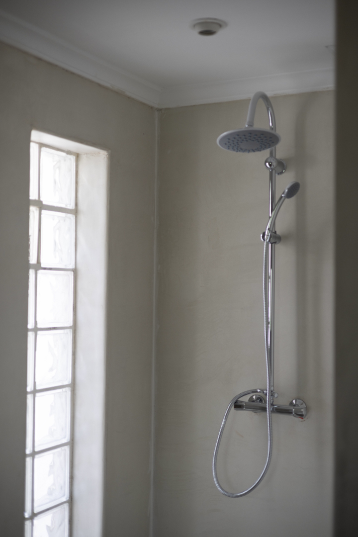 Détail de douche avec pomme de tête et fenêtre en pavés de verre dans une salle de bain aux murs crème.