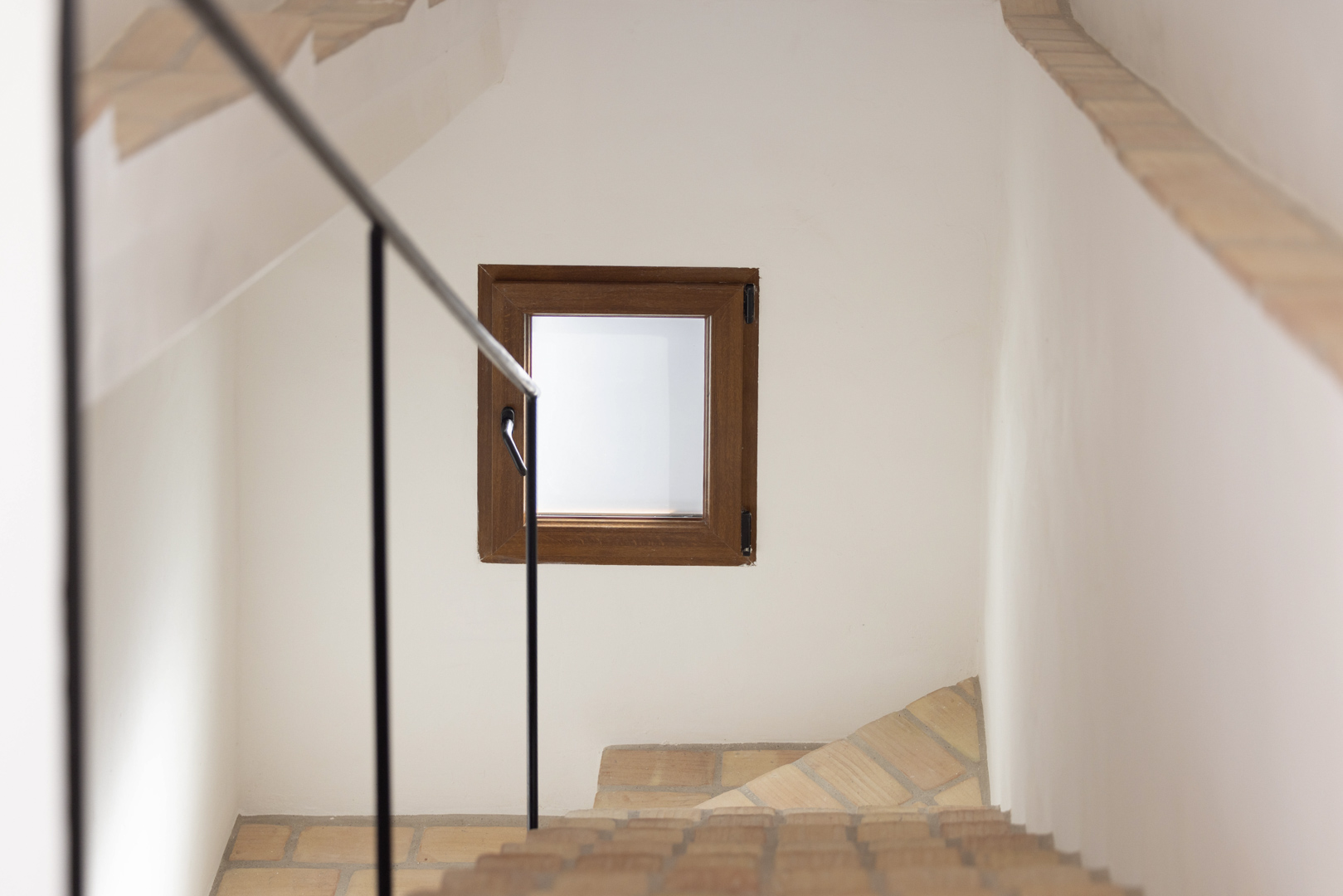 Détail d'escalier avec rampe noire et fenêtre en bois sur mur blanc.