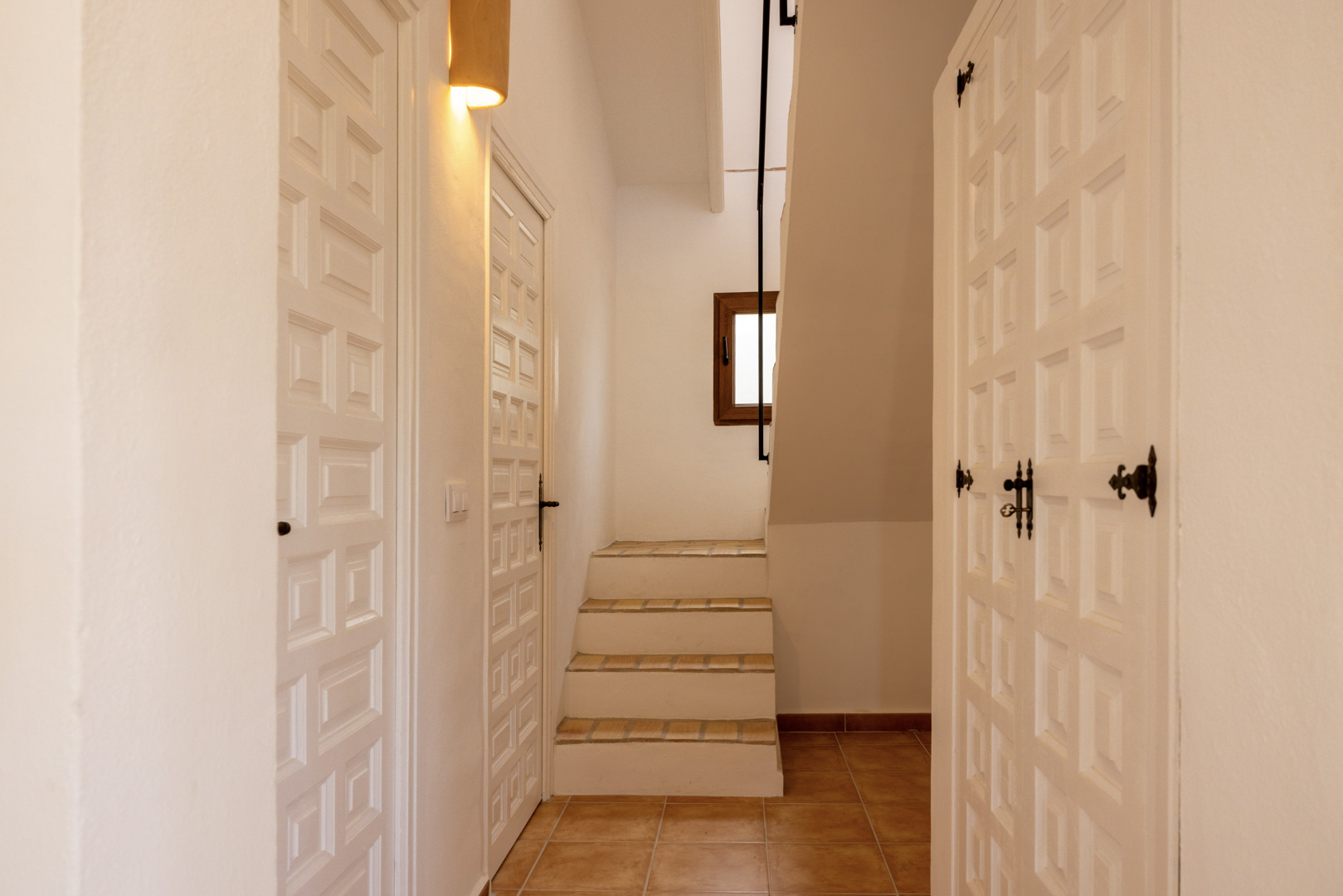 Détail du hall avec escalier carrelé et portes en bois blanc au design géométrique.