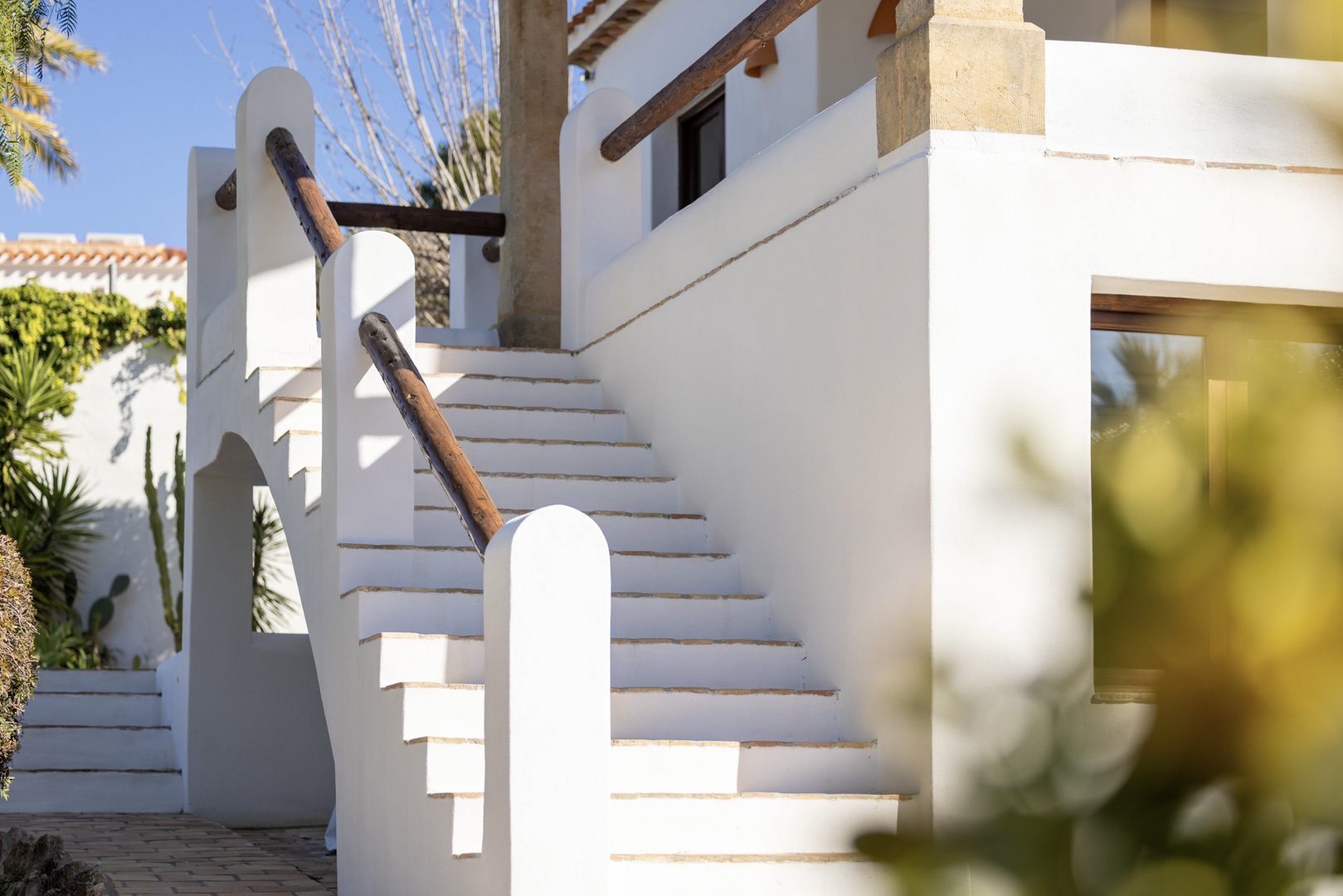 Détail d'un escalier extérieur blanc avec rampe en bois dans une villa à Jávea. Design méditerranéen lumineux.
