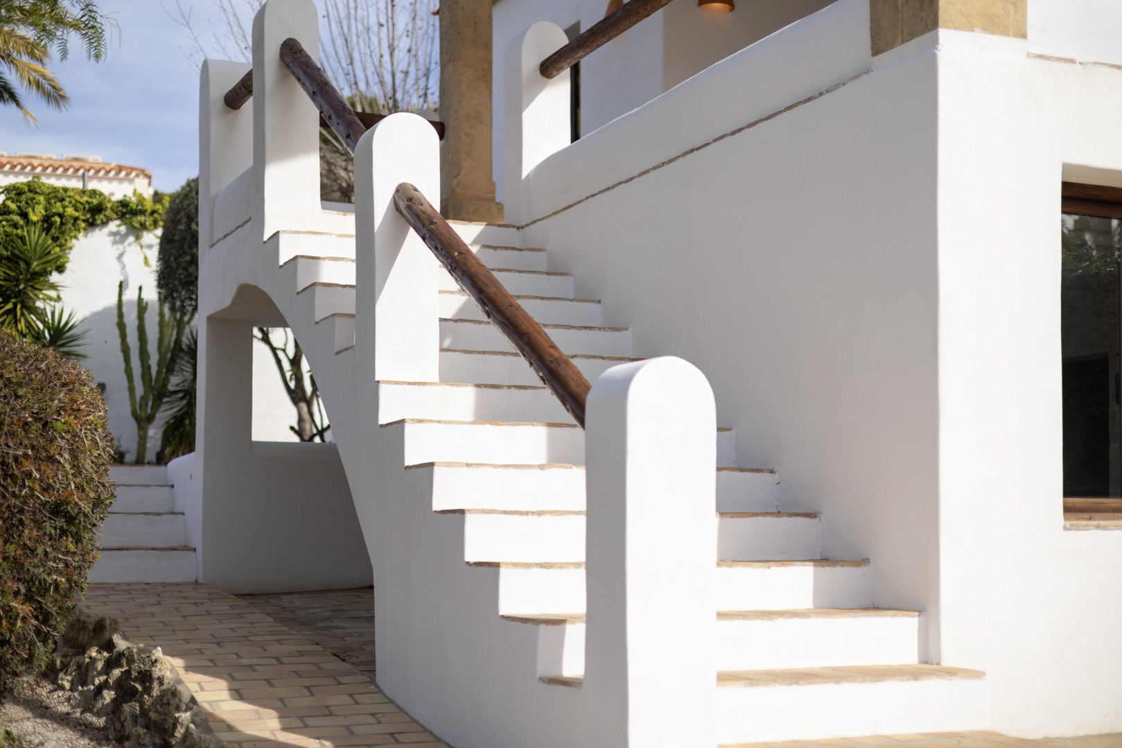Détail d'un escalier extérieur blanc avec rampe en bois et pavage en brique.