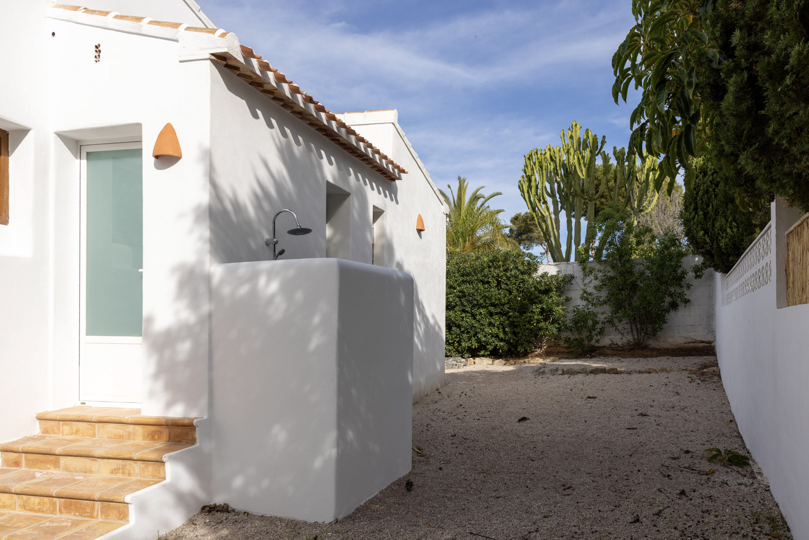 Extérieur de la villa avec douche extérieure et jardin de gravier avec végétation variée.